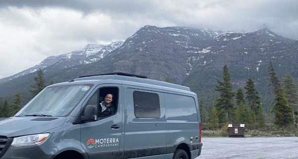 Woman Smiling from Driver’s Seat of Moterra Campervan Rental with Mountains in Background