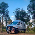 Two Women Kneeling and Smiling in Front of Moterra Campervan Rental on Vacation