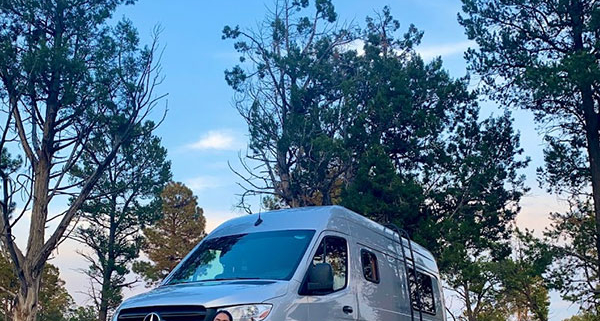 Two Women Kneeling and Smiling in Front of Moterra Campervan Rental on Vacation