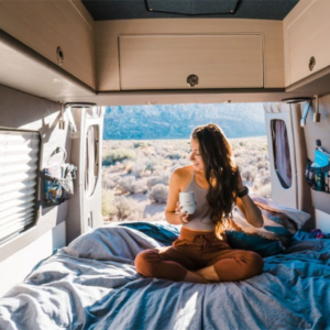 Young Woman Sitting Cross-Legged on Bed with Coffee Mug in Moterra Campervan Rental on Vacation