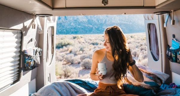 Young Woman Sitting Cross-Legged on Bed with Coffee Mug in Moterra Campervan Rental on Vacation