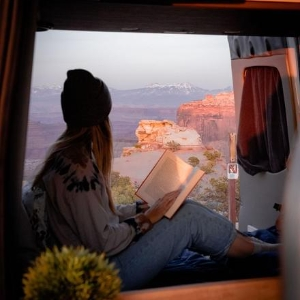Woman reading a book looking at the grand canyon in a campervan