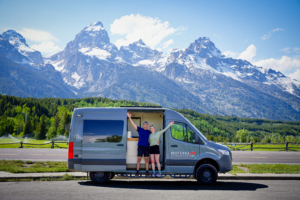 a happy couple in a campervan in front of the Grand Tetons